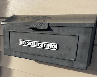 以下が含まれることがあります： 「NO SOLICITING」と書かれた白い看板が付いた黒い郵便受け。