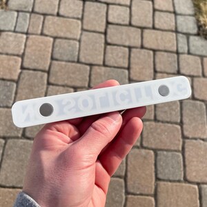 May include: White plastic magnetic strip with the text "ZOTICILOS" printed in black. The strip has two silver magnets on either end.