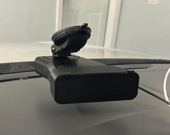 May include: A black dashcam with a suction cup mount is attached to a car's dashboard. The dashcam is rectangular with a small screen and buttons. The suction cup mount is black and holds the dashcam securely in place.