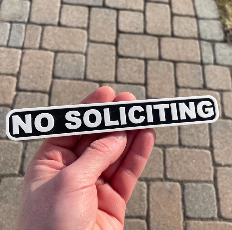 May include: A black and white sign with the text "NO SOLICITING" in white letters on a black background.