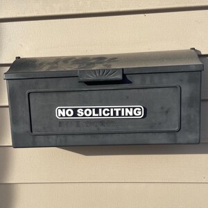 May include: A black mailbox with a white sticker that says "NO SOLICITING" on the front.