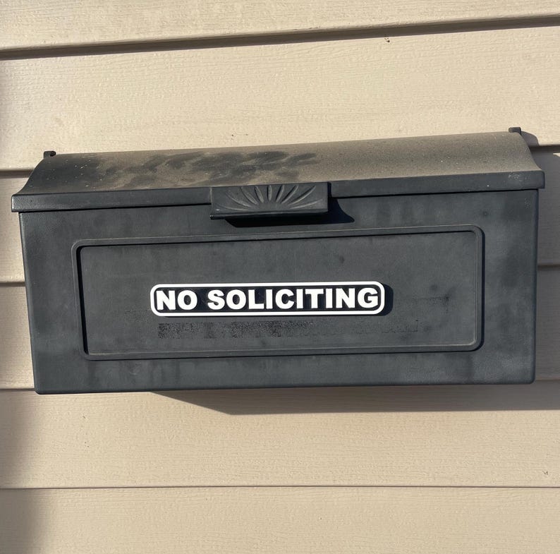 May include: A black mailbox with a white sticker that says "NO SOLICITING" on the front.