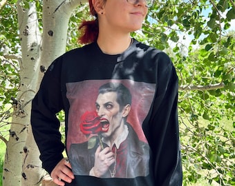 May include: Black sweatshirt with a graphic print of a man with a red rose in his mouth. The man is wearing a black suit and a white shirt with a red tie. The background is a red and black color.