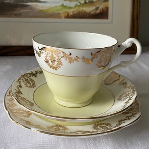 Puede incluir: Un juego de taza y platillo de té amarillo con ribetes dorados y diseños florales. El juego está hecho de porcelana fina y tiene un aspecto delicado y vintage.