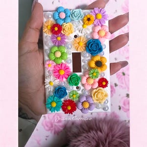 May include: White light switch cover decorated with colorful 3D flowers and pearls. The cover has the text "Jessica Carrasco" at the bottom.