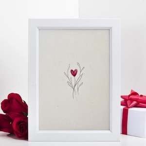 May include: A white framed art print featuring a red heart-shaped floral design. Beside the frame are three red roses and a white gift box with a red ribbon. The artwork is on a white background.
