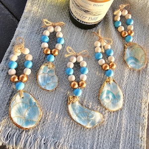 May include: Six blue and white oyster shell bottle stoppers with gold accents. Each stopper is decorated with a blue and white pattern and has a string of white and blue beads with gold beads.