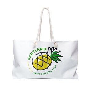 Può includere: Borsa tote bianca con manici in corda. La borsa presenta una grafica di ananas gialla e verde con il testo "Hartland Swim and Dive Team" in verde e giallo. La borsa è progettata per il trasporto di oggetti.