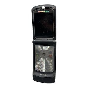 Könnte beinhalten: Ein schwarzes Motorola Razr Klapphandy in geöffneter Position. Das Gerät verfügt über einen dunklen Bildschirm im oberen Bereich mit dem Motorola-Logo darüber sowie eine metallische Tastatur mit einer runden Navigationstaste.