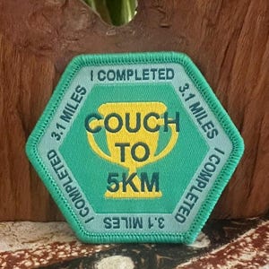 May include: A green and yellow embroidered patch with the text "COUCH TO 5KM" and "I COMPLETED 3.1 MILES". The patch is in a hexagon shape with a teal border and a gold trophy graphic.