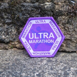 May include: A purple Ultra Marathon patch with white text and a runner graphic. The hexagonal patch reads "ULTRA MARATHON" and has a stitched border.