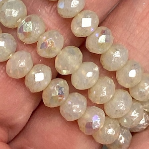 May include: Close-up of iridescent, faceted beads. The beads are oval-shaped and have a pearlescent, shimmering quality. The beads are strung together, suggesting they are for jewelry making or crafting.