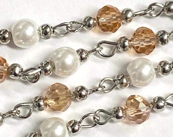 Op de afbeelding: Close-up van een kralenketting met afwisselend witte parel kralen en facetgeslepen amberkleurige kristallen kralen. De kralen zijn geregen op een zilveren ketting, wat een delicaat ontwerp creëert. De achtergrond is wit.