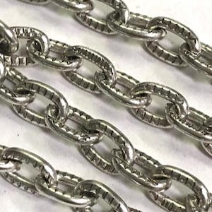 May include: Close-up of several silver-colored chains. Each oval link has a textured, patterned surface. The chains are arranged diagonally across the frame, creating a sense of depth and detail. The image is well-lit, highlighting the metallic sheen.