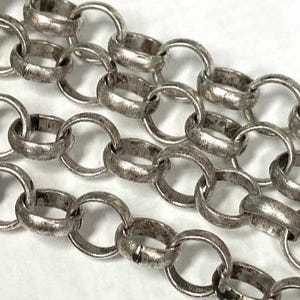 Könnte beinhalten: Nahaufnahme einer silbernen Kette mit großen, ovalen Gliedern. Die Kette hat ein abgenutztes, antikes Aussehen mit sichtbarer Textur und leichter Verfärbung. Die Glieder sind ineinander verschlungen und bilden ein Muster.