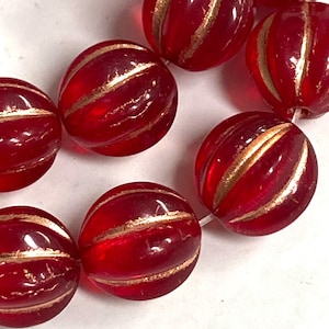 Puede incluir: Primer plano de un collar de cuentas de vidrio rojas con rayas doradas. Las cuentas redondas tienen una textura acanalada. Las rayas doradas añaden un toque de elegancia. Ideales para la creación de joyas.