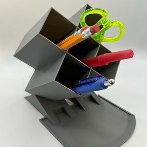 May include: A gray plastic desk organizer with multiple compartments. The organizer is filled with office supplies, including pencils, pens, and a pair of green scissors.