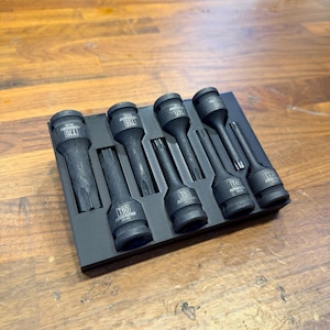May include: A set of black Torx bit sockets in a black tray. The sockets are labeled with sizes T70, T60, T55, T50, T47, T45, and T30. The tools are arranged neatly on a wooden surface.