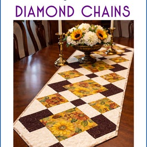 Puede incluir: Camino de mesa acolchado con un patrón de cadena de diamantes. El camino de mesa presenta cuadrados alternos de tela floral con girasoles y tela marrón. El texto "Glory Quilts" y "Diamond Chains" son visibles.