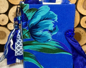 May include: A blue fabric-covered journal with a floral design featuring blue and green tulips. The journal has a blue ribbon and a blue tassel with silver beads.
