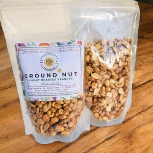 Puede incluir: Dos bolsas de pl&aacute;stico transparentes llenas de cacahuetes tostados. Las bolsas est&aacute;n etiquetadas con "GROUND NUT YUMMY ROASTED PEANUTS" y "Made with Love". El texto tambi&eacute;n dice "Hygienically sourced in Nigeria" y "Packaged in the USA".