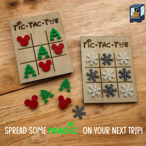 May include: Wooden Tic-Tac-Toe game sets with laser-cut designs. One set features red Mickey Mouse heads and green Christmas trees, the other has white and gray snowflakes. The text reads "SPREAD SOME MAGIC ON YOUR NEXT TRIP!"
