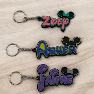 Three mouse inspired name keychains are shown. All keychains will come in with 3 layers for a sleek, sturdy finish. The bottom layer will be black, but the middle and top layers are available in 15 different color options. All keychains are made custom to order.