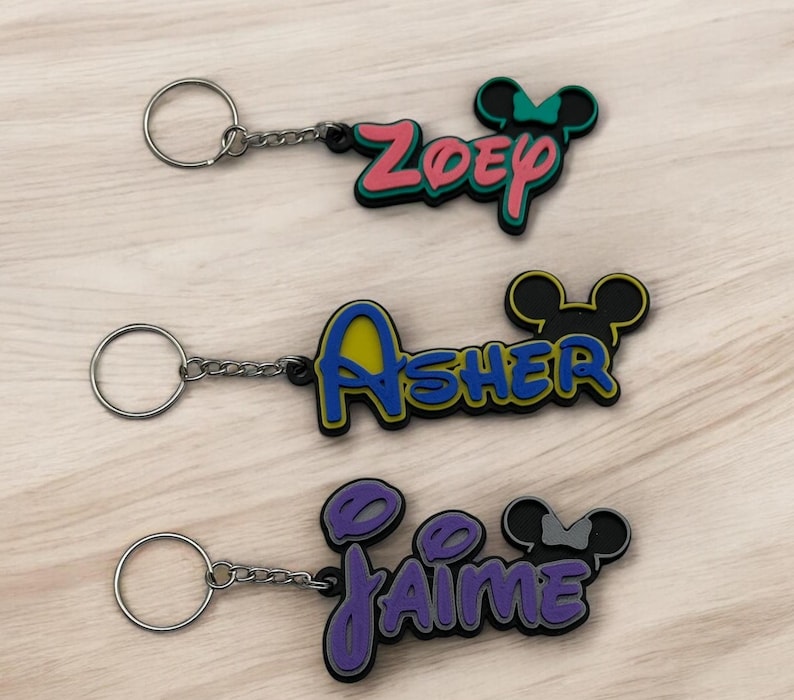 Three mouse inspired name keychains are shown. All keychains will come in with 3 layers for a sleek, sturdy finish. The bottom layer will be black, but the middle and top layers are available in 15 different color options. All keychains are made custom to order.