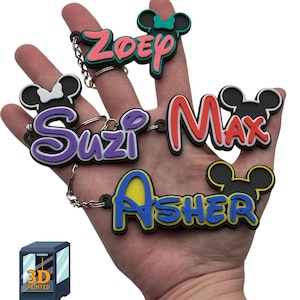 May include: Four 3D printed keychains with Mickey Mouse ears. The keychains are in different colors and feature the names "Zoey", "Suzi", "Max", and "Asher".