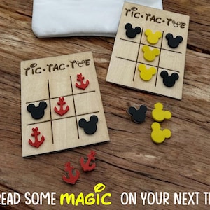 May include: Two wooden tic-tac-toe boards with Mickey Mouse ears and anchors as game pieces. The boards are on a wooden surface. The text "TIC-TAC-TOE" is printed on each board. The text "SPREAD SOME MAGIC ON YOUR NEXT TRIP!" is printed below the boards.