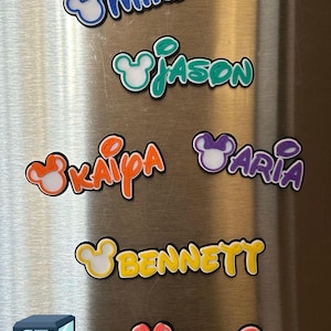 May include: Five colorful 3D printed name magnets with a Mickey Mouse ear design. The names are Mike, Jason, Kaipa, Aria, and Bennett. A sixth magnet with the name Monica is pink and is partially visible at the bottom of the image.