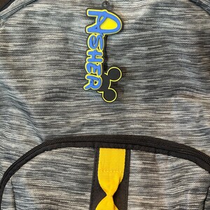 An example of a boy keychain hanging off a backpack. The keychain is attached to the zipper of the backpack.