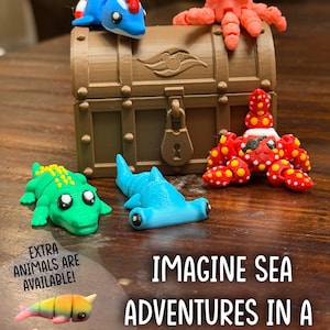 May include: A brown plastic treasure chest with a central lock and embossed emblem, surrounded by articulated 3D-printed sea creatures including a pink octopus, blue dolphin, green alligator, blue hammerhead shark, and a red spotted crab.