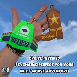 May include: Two keychains featuring the word BELIEVE. One is a bright green space-themed chest plate with purple and red accents. The other is a brown cowboy boot with a yellow star badge and yellow strap. Both have metal rings for attachment.