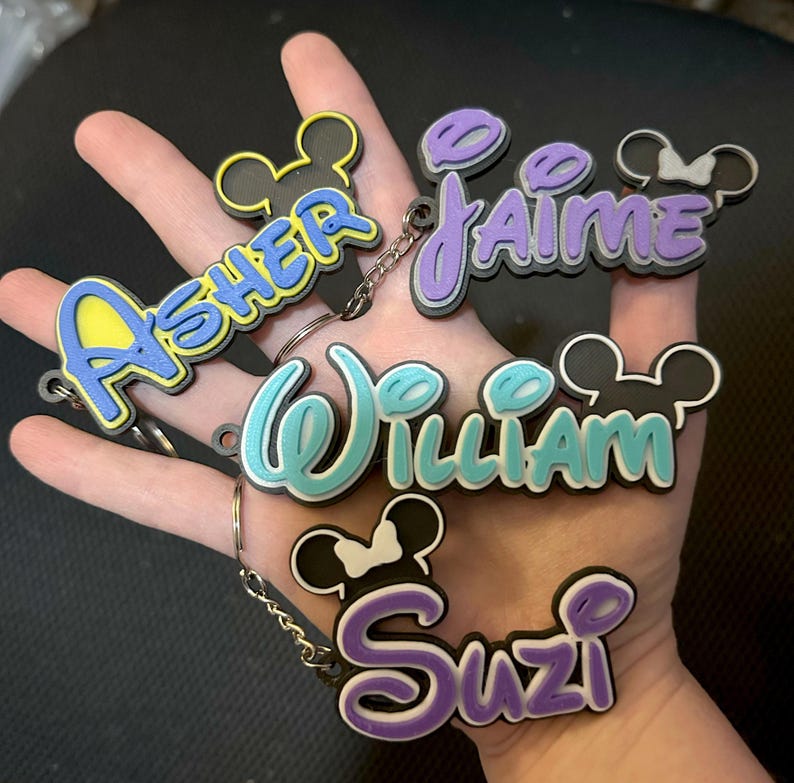 4 Personalized Mouse Inspired Name Keychains in various colors. 2 girl versions and 2 boy versions are shown for examples. The keychains will have a mouse head included for the boy option and girl versions will have a bow included.