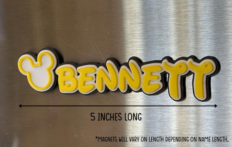 A yellow and black custom name magnet with the name 'BENNETT' in a mouse inspired font. This magnet example is 5 inches long and includes a Mouse head design on the left of the name. *Magnets will vary on length depending on name length.