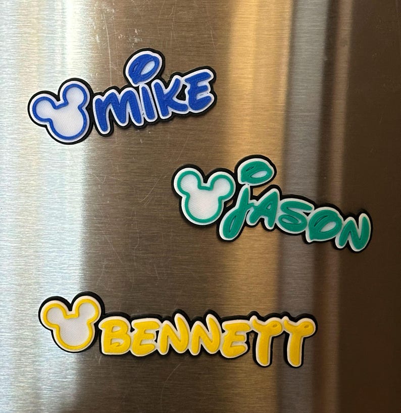 Three personalized name magnets with a Mouse head design in the boy version. The magnets are in blue, green, and yellow. Each magnet will have 3 layers: black bottom layer, white middle layer and your choice of color for the top layer.