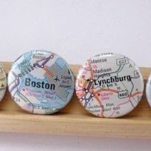 Puede incluir: Cuatro botones redondos con mapas de diferentes ciudades. Los botones son blancos con texto negro y líneas. Las ciudades son Lansing, Boston, Lynchburg y Holland.