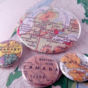 Puede incluir: Cuatro botones redondos y coloridos con mapas de diferentes lugares. Los botones son amarillos, rojos, azules y verdes. Los mapas muestran las ubicaciones de Budapest, Hungría; Detroit, Michigan; Atenas, Grecia; y Yukón, Canadá.