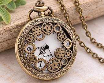 May include: A bronze-toned pocket watch with a white face, black hands, and a gear-themed skeleton design. The watch features a circular case with decorative engravings and is attached to a matching bronze-toned metal chain link necklace.