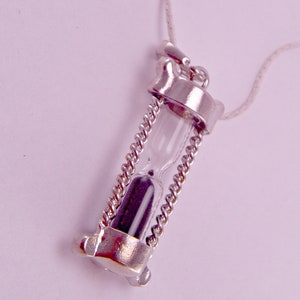May include: A silver necklace with an hourglass pendant. The hourglass is filled with black sand and has a clear glass tube.