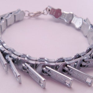 May include: A silver bracelet made from a series of connected zipper pulls.