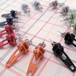 May include: Assortment of colorful zipper pull earrings. The earrings are made from metal and plastic and feature a variety of colors, including red, orange, black, green, and blue.