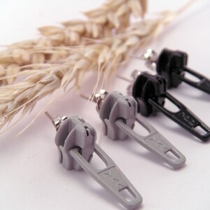 May include: A pair of earrings featuring a zipper design. One pair is gray and the other is black.