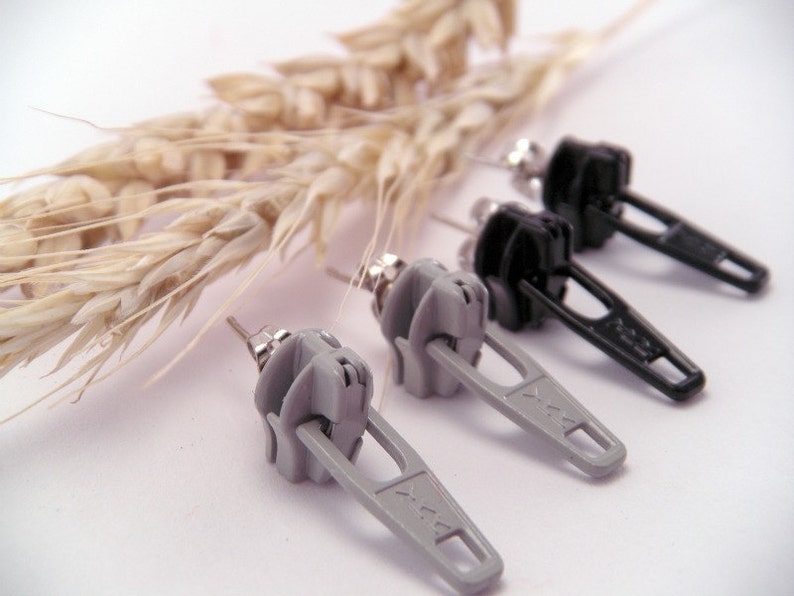 May include: A pair of earrings featuring a zipper design. One pair is gray and the other is black.