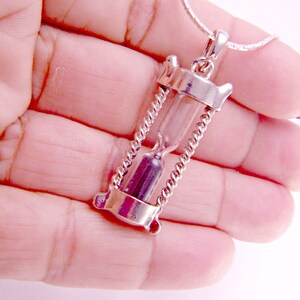May include: A silver hourglass pendant necklace with a clear glass hourglass and a silver chain.