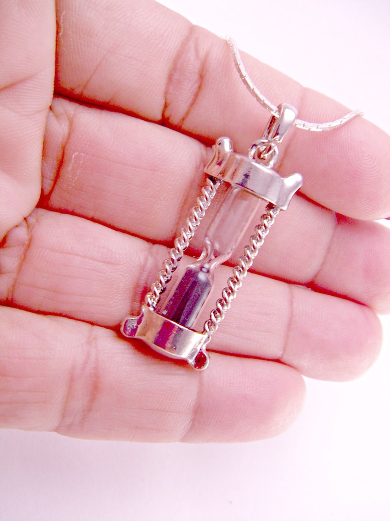 May include: A silver hourglass pendant necklace with a clear glass hourglass and a silver chain.