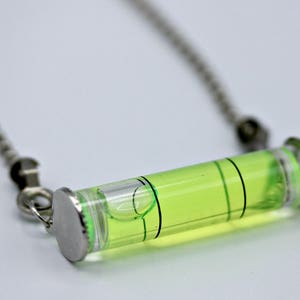 May include: A silver chain necklace with a green glass level pendant. The level is filled with a green liquid and has a black line in the middle.