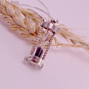 May include: A silver necklace with a small hourglass pendant. The hourglass is filled with black sand and is suspended from a delicate chain.