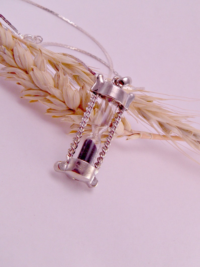 May include: A silver necklace with a small hourglass pendant. The hourglass is filled with black sand and is suspended from a delicate chain.